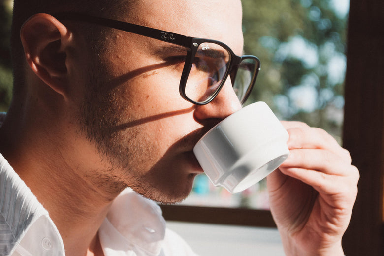 Man wearing glasses drinking out of espresso mug in front of a window